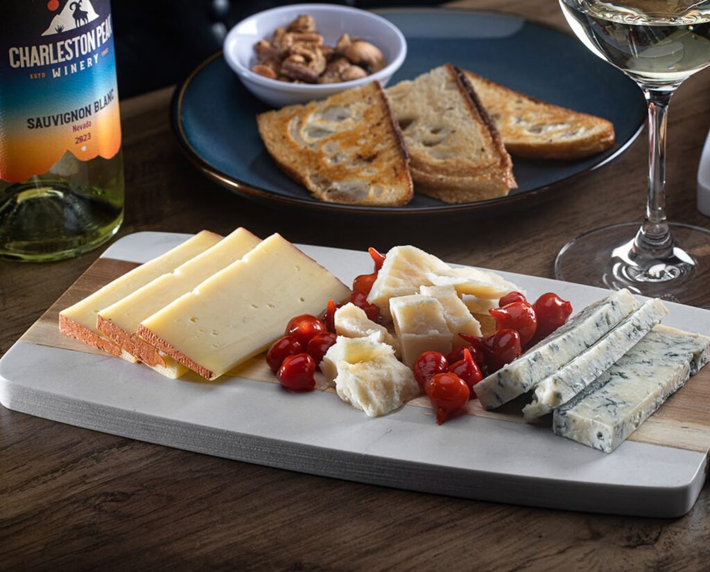 Photo of a assorted cheeses, toasted bread, and a bottle Charleston Peak Sauvignon Blanc wine